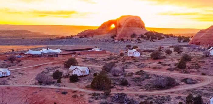 Aerial view of the campground at Ulum Moab, showcasing several large, widely spaced tents connected by a dirt road.