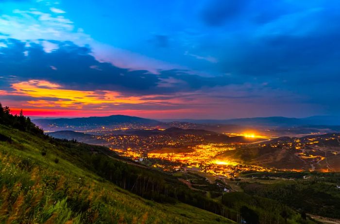 A vibrant sunset casts colorful reflections over the lights of Park City, Utah, viewed from a ski lift