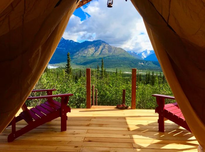 A view of the forest and distant mountains from the wooden deck of a tent, complemented by two red Adirondack chairs.