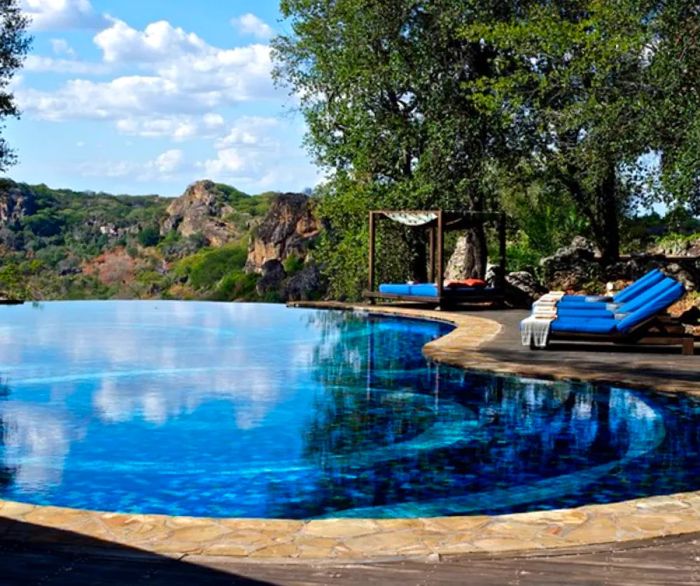 The curved swimming pool at Singita Pamushana Lodge in Zimbabwe, surrounded by blue lounge chairs with sweeping views of the landscape.