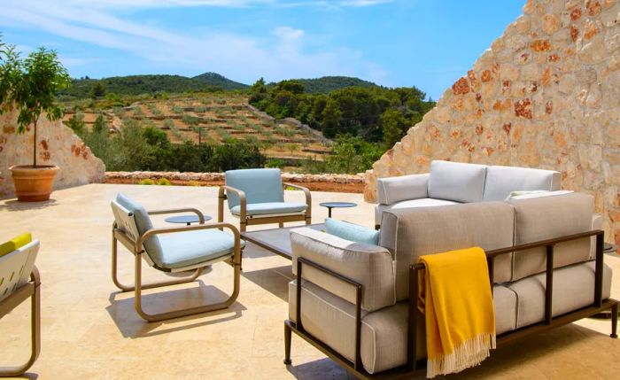 Pastel-colored cushioned chairs and sofas outdoors at Villa Nai 3.3 Hotel, overlooking green fields and trees in the distance.