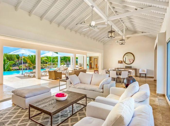 A spacious, white living and dining area in St. Martin, featuring a wall of windows that opens up to the pool.