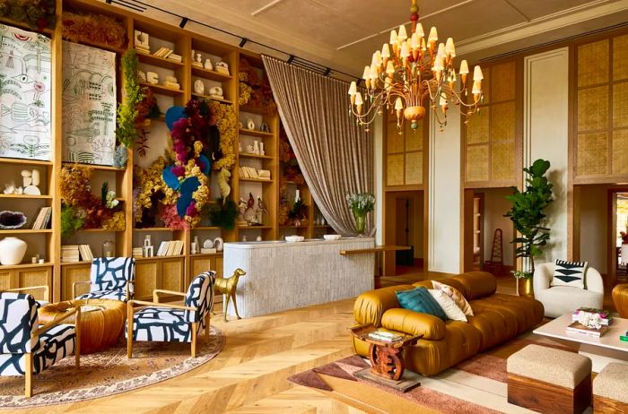 A lobby featuring contemporary low couches, patterned chairs, flowing curtains, wooden flooring, and a chandelier.