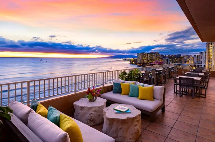 Outdoor terrace at Twin Fin's Coconut Club, featuring sofas with a stunning sunset view over the Pacific Ocean.