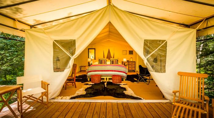 View of a white tent interior featuring a bed and chairs, as seen from a wooden deck.