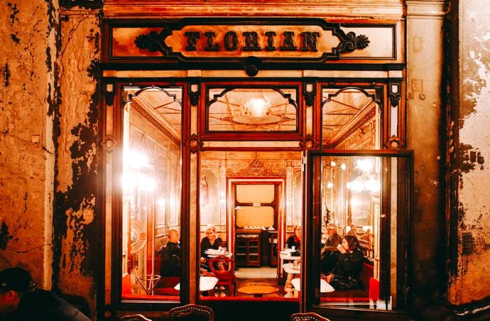 A cozy café interior in Venice, softly illuminated, filled with people at small tables