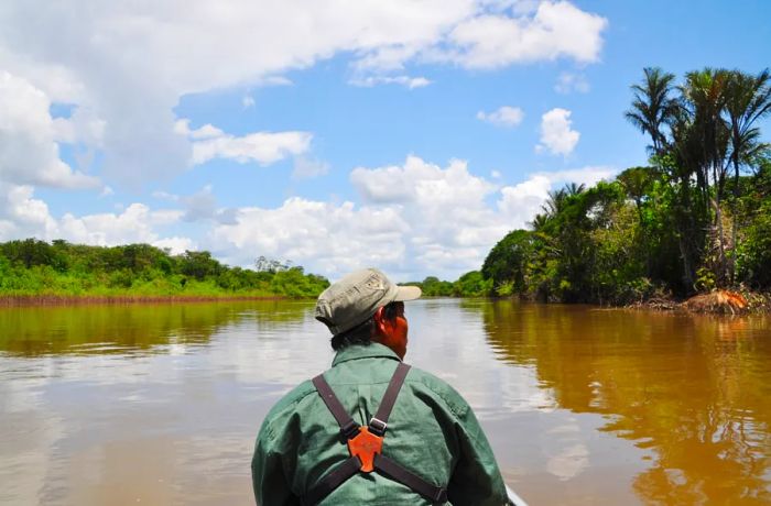 The back view of a man steering a boat along a broad, muddy river