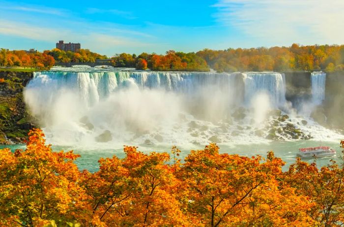 Niagara Falls framed by vibrant orange trees, with a tour boat at the base of the majestic falls.