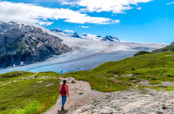 A female hiker traverses the Harding Icefield trail in Kenai Fjords National Park, with Exit Glacier visible in the background.