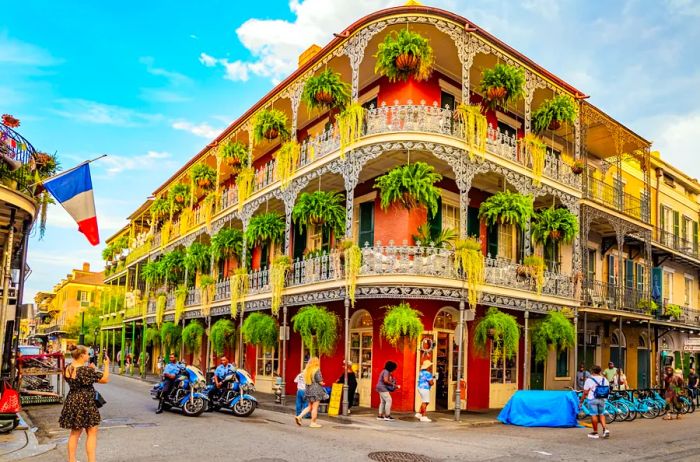 A stunning Creole townhouse commands attention at a street corner in New Orleans' French Quarter, featuring two tiers of balconies adorned with lush hanging plants.