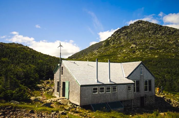 A rustic wooden shelter hut nestled among lush green hills in New Hampshire's White Mountains.