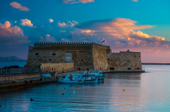 A stunning sunrise casts its glow over a fortress, with boats gently bobbing in the water.