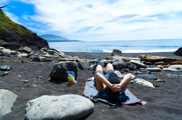 A young woman hiker relaxing on a black sand beach