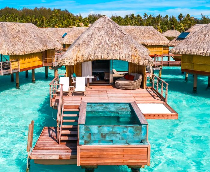 Picture a wooden deck and plunge pool of a thatched-roof overwater bungalow, nestled among several others.