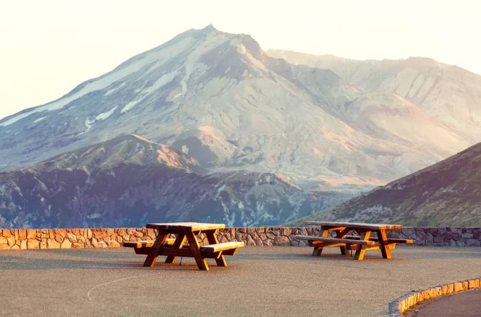 Mount St. Helens in Washington featuring two wooden picnic tables in the foreground.