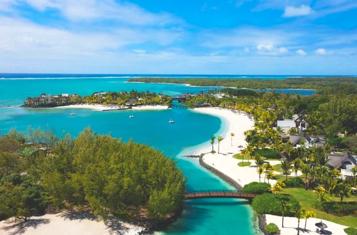 An aerial perspective showcasing winding white-sand beaches framed by lush greenery and a few low-rise buildings nearby.