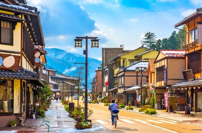 A charming street in Yamanaka Onsen, Japan, lined with quaint tan and yellow buildings, featuring a cyclist in the foreground.