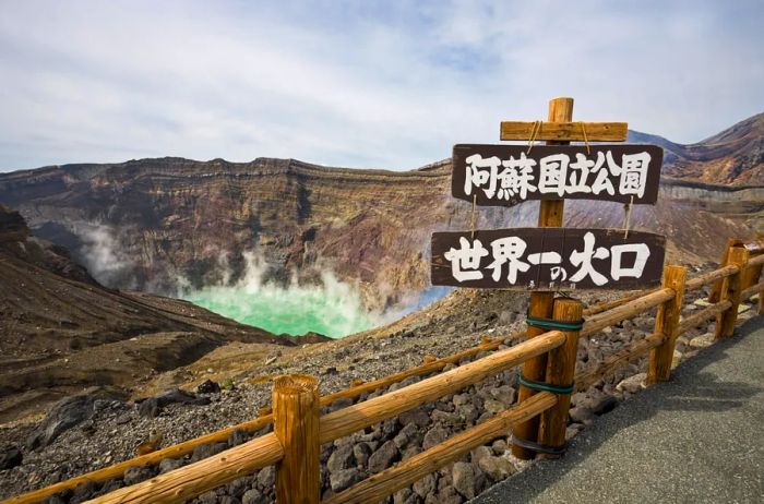 A wooden sign with white Japanese characters beside steaming green waters in the rocky brown caldera of Mount Aso.