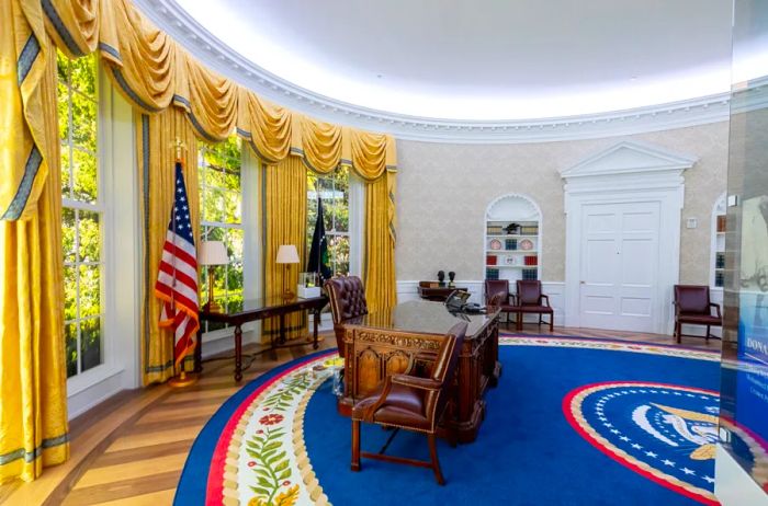 The Oval Office adorned with a vibrant seal carpet, the American flag, opulent golden curtains, and a wooden desk paired with a leather chair.