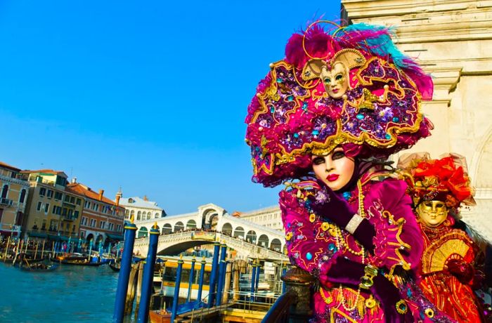 Two individuals dressed in vibrant-colored dresses posing in front of a canal in Venice.