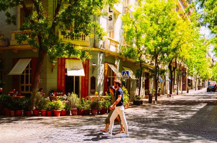 A couple enjoys a sunny stroll along a cobblestone street in the Salamanca district of Madrid, Spain.