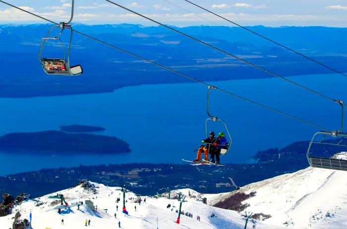 Two skiers enjoying a chairlift ride above a snow-covered mountain with a lake in the distance