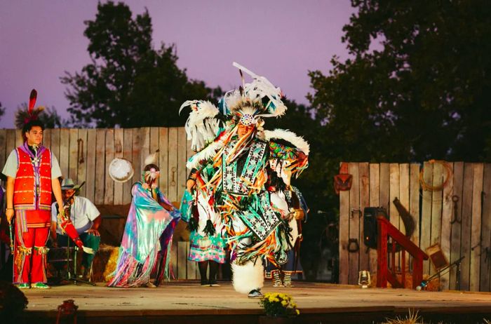 A night performance featuring Plains Indian dancers on an outdoor stage at the Oklahoma State Fair.