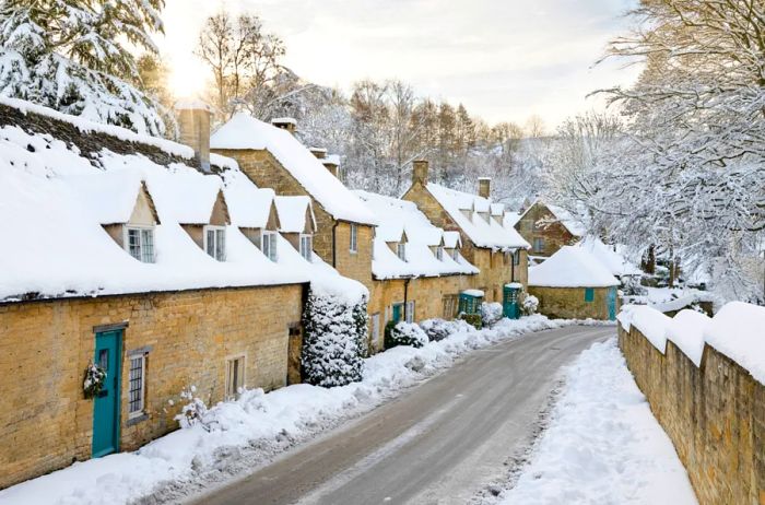 A row of stone cottages blanketed in winter snow lining a narrow road