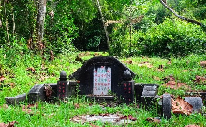 A tomb adorned with vibrant red and green Chinese characters, encircled by lush grass and trees at a cemetery in Singapore.