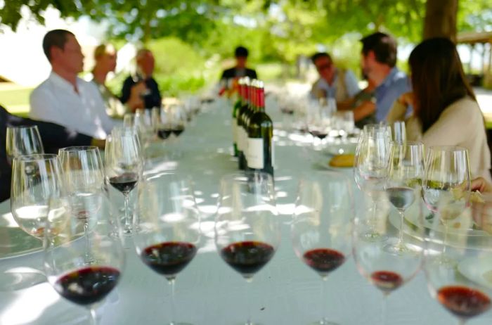 A group enjoying a leisurely red wine tasting at an outdoor table adorned with a white tablecloth in Bordeaux, France.