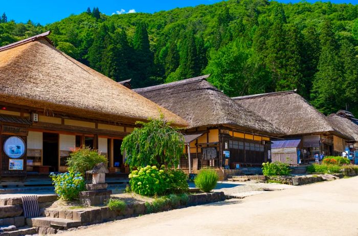 Ishiharaya, a charming teahouse in Ouchi Juku, nestled among a row of one-story thatched-roof shops, with a backdrop of lush green hills.