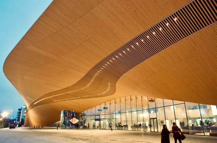 A gracefully curved wooden roof extends over the high windows of the Oodi public library's exterior.