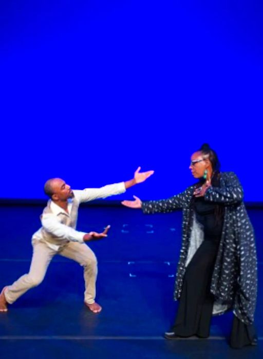 A couple, Glenis Redmond and Vaughn Newman, performing together on a vibrant blue stage in Asheville.