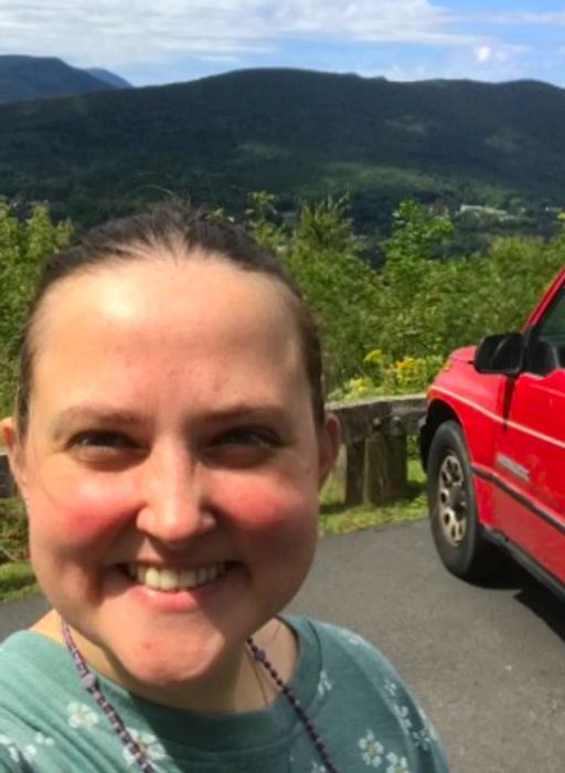 Close-up of a woman beaming next to her parked red car at a viewpoint on the Blue Ridge Parkway