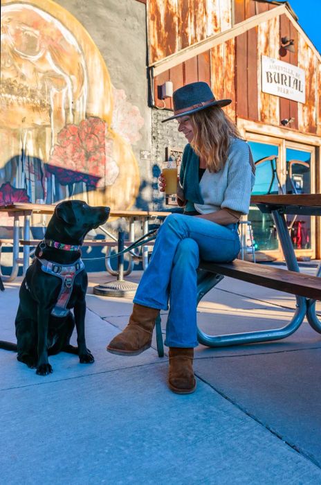 A black dog watches their human companion enjoying a drink on the outdoor patio at Burial Beer.