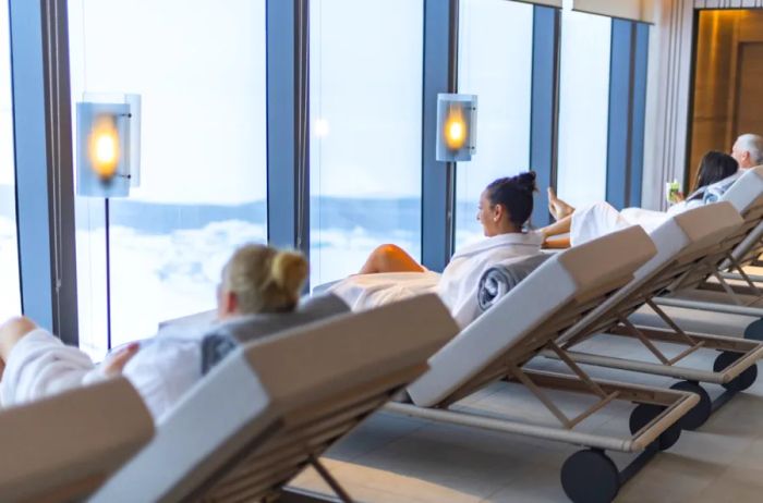 Guests relaxing on lounge chairs in spa attire, gazing out the window of a cruise ship.