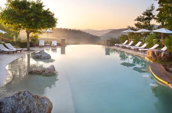 An outdoor infinity pool with a curved design, surrounded by empty white lounge chairs and umbrellas.