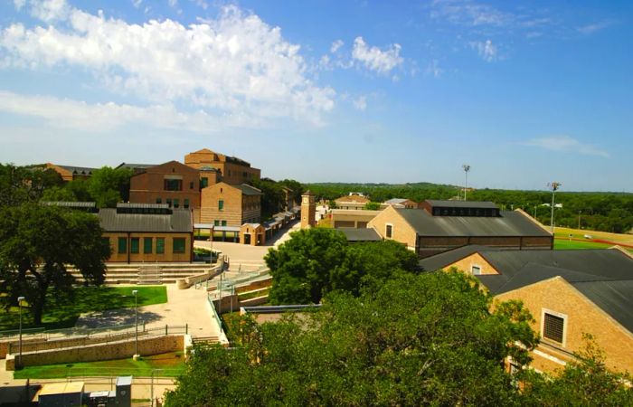 An aerial view of the Texas School for the Deaf in Austin reveals a campus with numerous light-colored brick buildings surrounded by lush green grass and trees.