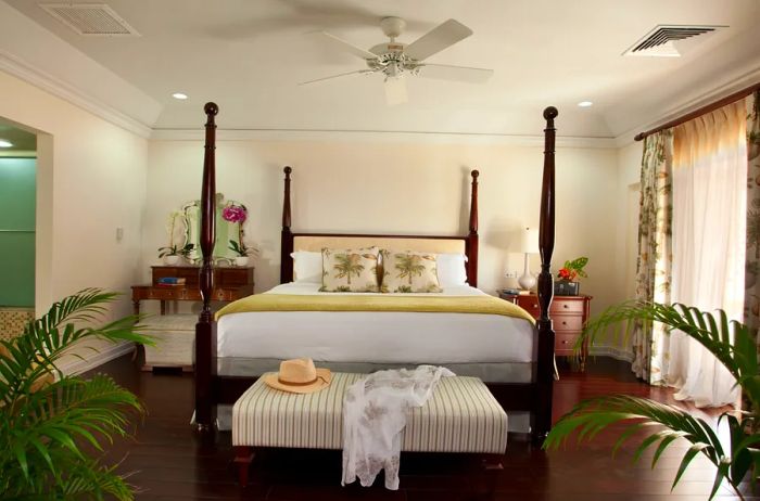 A Grand Luxury Oceanfront Suite at BodyHoliday in St. Lucia, featuring a four-poster bed, wooden floors, a ceiling fan, and white walls.