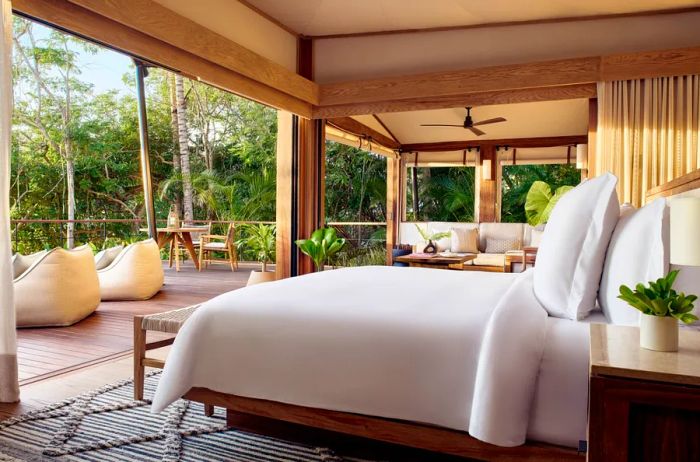 A tent-style hotel room showcasing a king-size white bed, with sliding glass doors that open onto a spacious wooden patio.