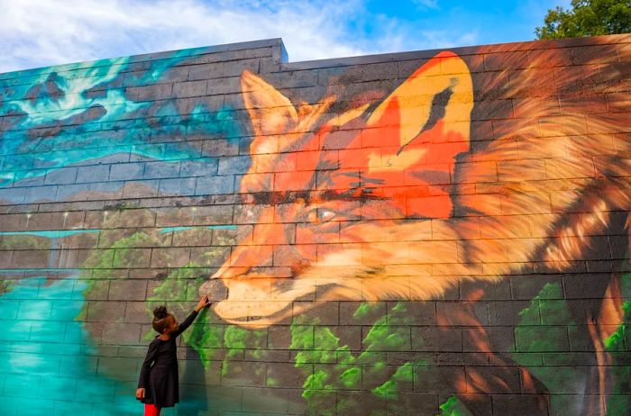 A young girl extends her hand to touch the nose of a fox depicted in a mural by artist Gus Cutty.