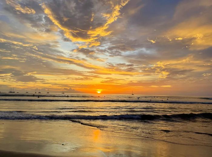 A stunning sunset over Tamarindo beach in Costa Rica, with silhouettes of ships and surfers in the distance.