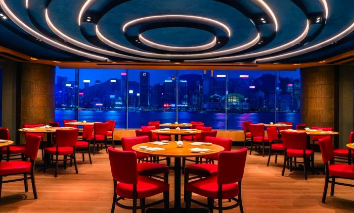 Nobu Hong Kong, located within the Regent Hong Kong, features striking crimson chairs, elegant blond wood flooring, and breathtaking views of Victoria Harbour, particularly enchanting at night.