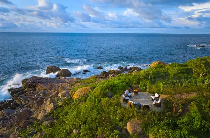 A cozy firepit surrounded by six chairs sits on a small circular deck overlooking the Pacific Ocean.