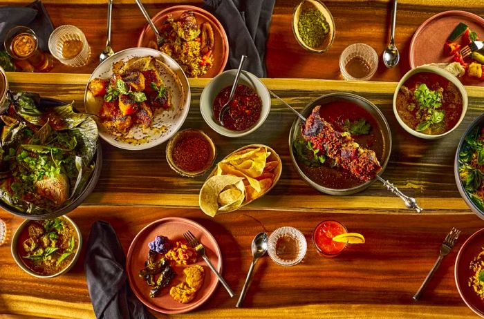 Aerial view featuring an array of small plates and bowls filled with food and spices arranged on a wooden tabletop at Buccan restaurant.