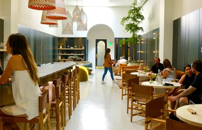 A stylish gray and white interior at Marine Layer Wines, featuring a guest at the bar on the left and several patrons at round tables on the right.