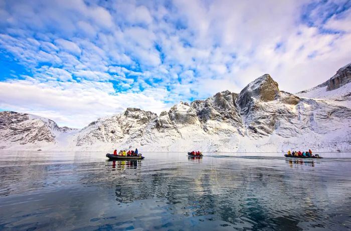 Three Zodiacs filled with people navigate the waters in Arctic Canada, surrounded by snow-capped peaks in the background.