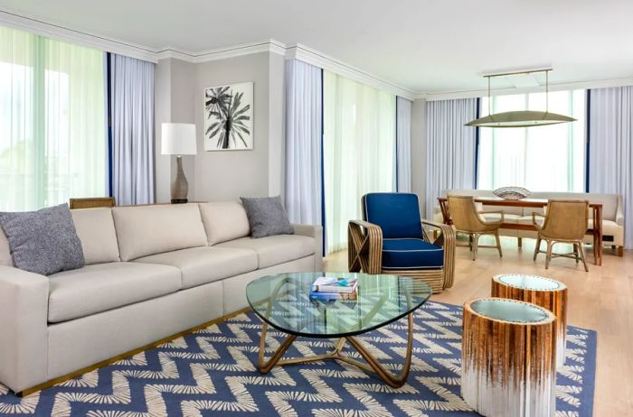 The living room of a suite at the Ritz-Carlton Coconut Grove in Miami features a striking blue and white zigzag carpet, a spacious white sofa, and expansive floor-to-ceiling windows.