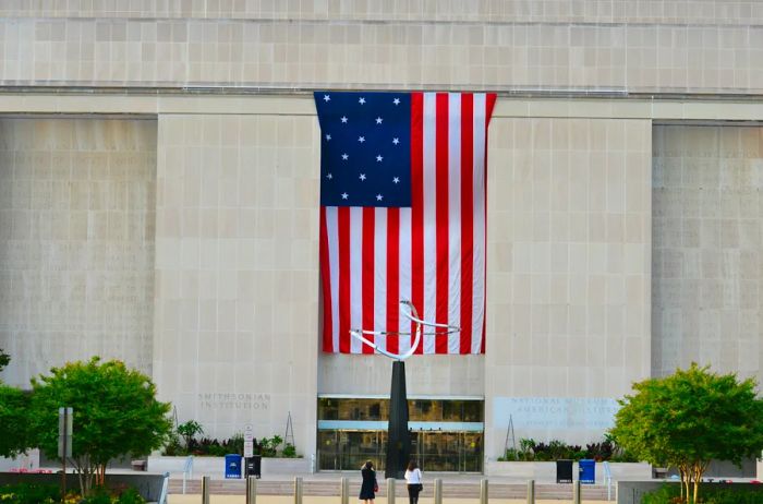 View of the entrance to the National Museum of American History, featuring a vertical U.S. flag and a sleek silver abstract sculpture.