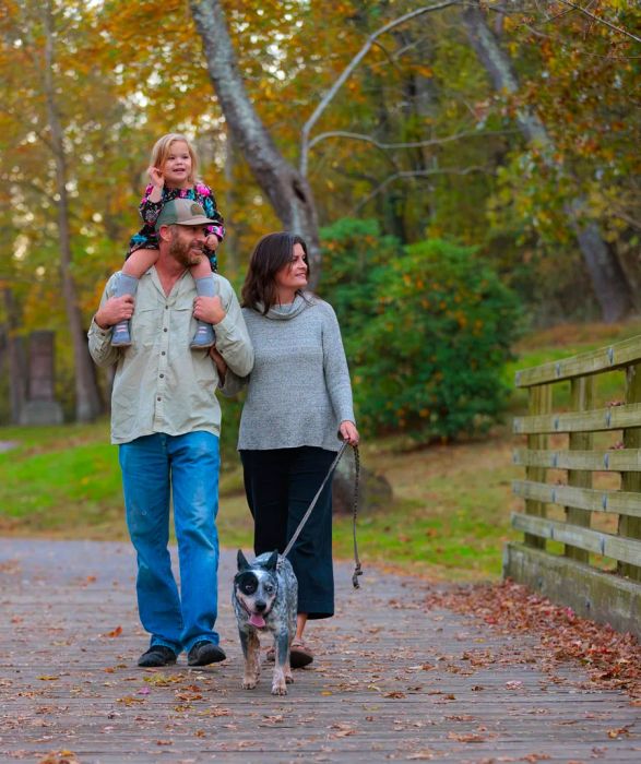 A family strolls with their dog on Reed Creek Greenway in Asheville, with the dad balancing a child on his shoulders.